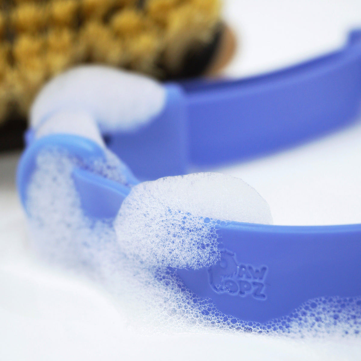 PawPopz Halsband in blau fokus auf Logo rein geprägt mit Schaum Abwaschbar eine bürste unscharf im hintergrund 
