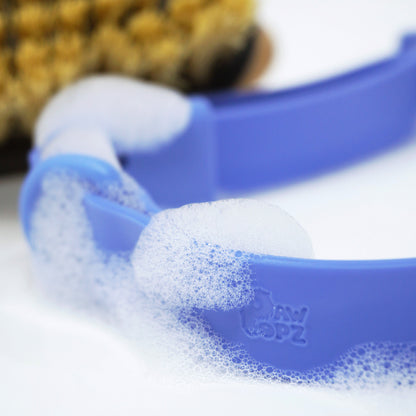 PawPopz Halsband in blau fokus auf Logo rein geprägt mit Schaum Abwaschbar eine bürste unscharf im hintergrund 